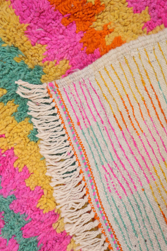 Tapis berbère coloré avec des motifs géométriques en rose, orange, jaune et vert, tissé à la main avec des franges.