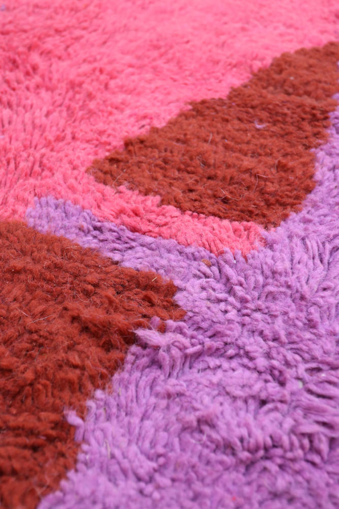 Tapis berbère coloré avec des motifs géométriques en rose, violet et marron, ajoutant une touche moderne à votre décoration.