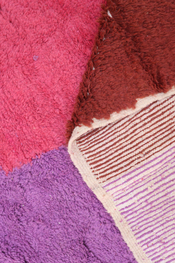Tapis berbère aux teintes vives de rose, violet et brun avec des motifs rayés et texturés.