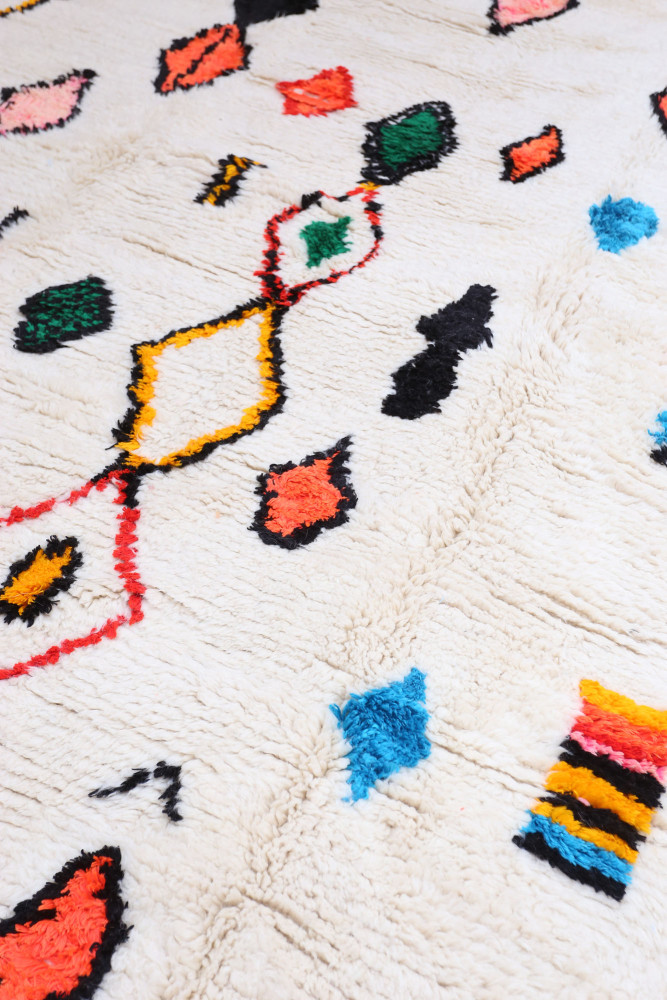 Tapis berbère aux motifs géométriques colorés, combinant des teintes blanches, noires, rouges, vertes et bleues.