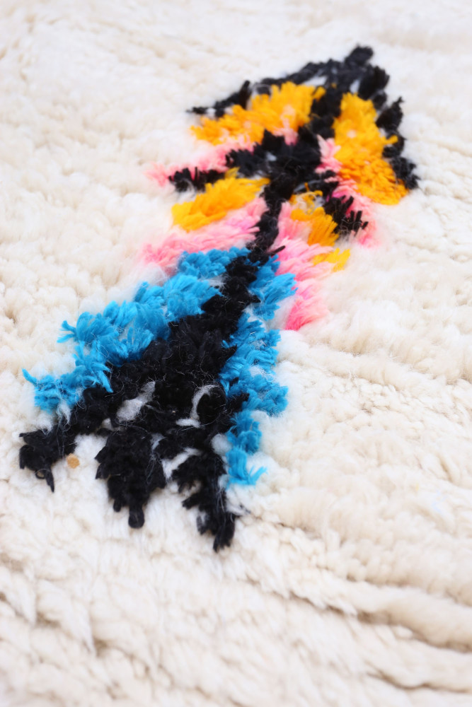 Tapis berbère aux motifs colorés avec des teintes de noir, bleu, jaune et rose sur un fond crème doux.