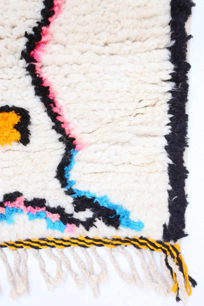 Tapis berbère en laine, aux motifs géométriques colorés avec des nuances de blanc, noir, rose et bleu.
