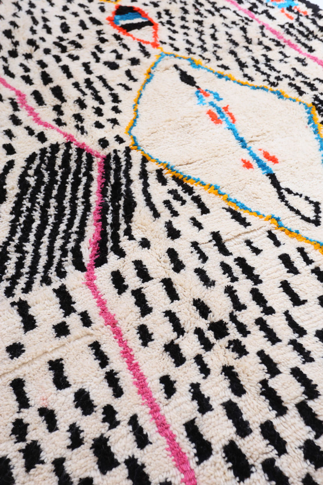 Tapis berbère moderne avec motifs géométriques en noir, rose, orange et bleu sur un fond crème.