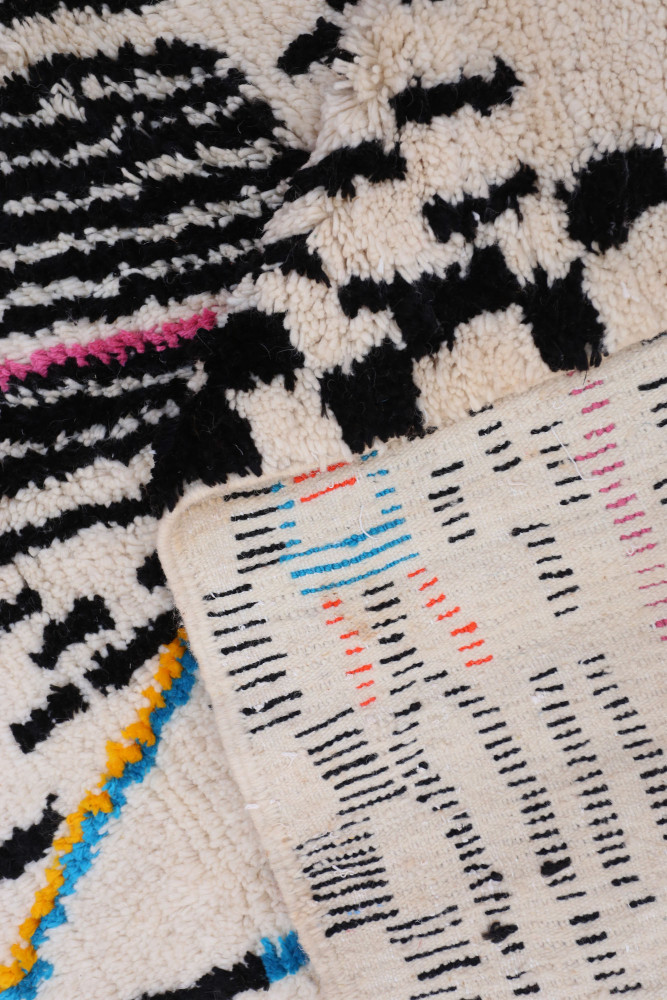 Tapis berbère au design moderne, présentant des motifs géométriques en noir, beige et accents de couleurs vives.
