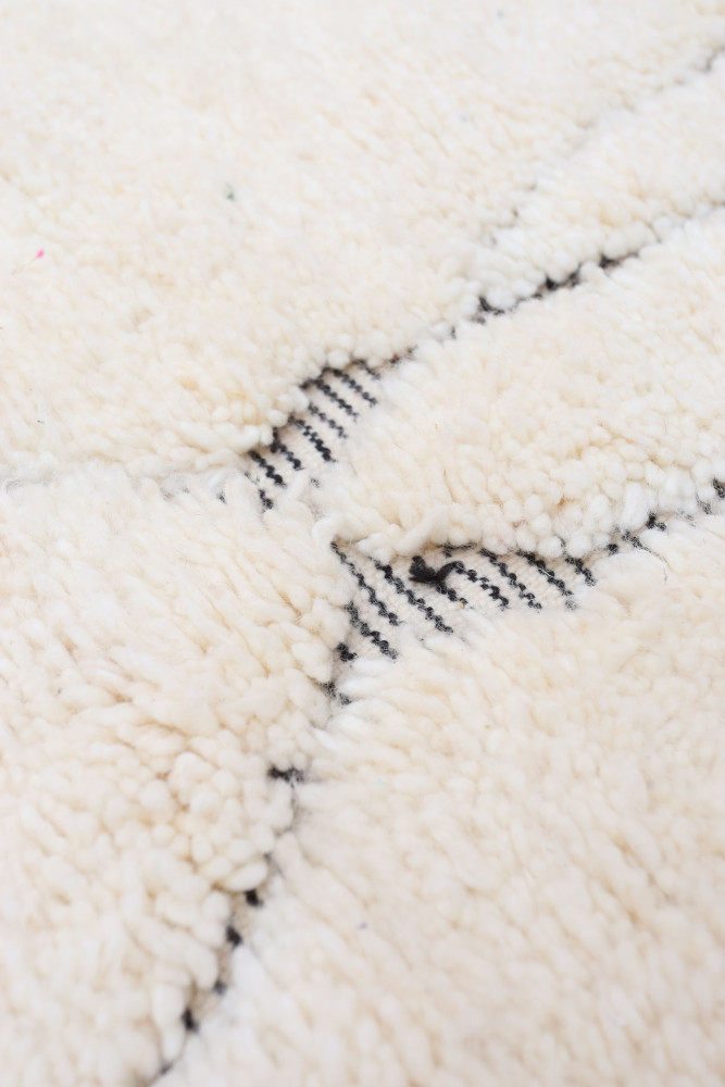 Tapis berbère en laine, couleur crème avec des motifs géométriques noirs et une texture douillette.