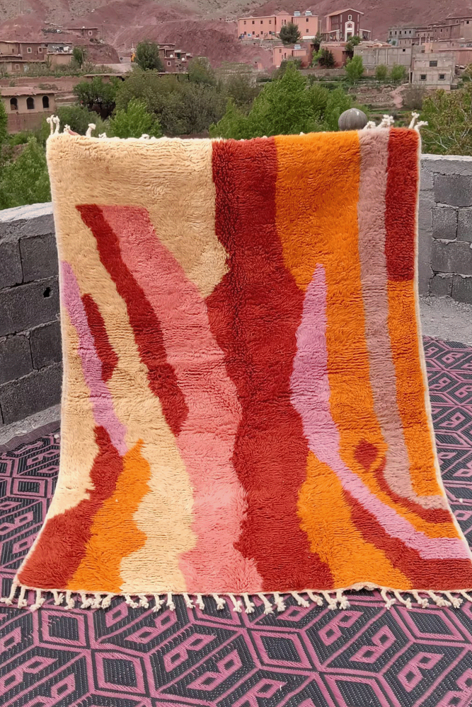 Tapis berbère au design moderne, aux couleurs vives d\'orange, rose et beige avec des motifs abstraits fluides.