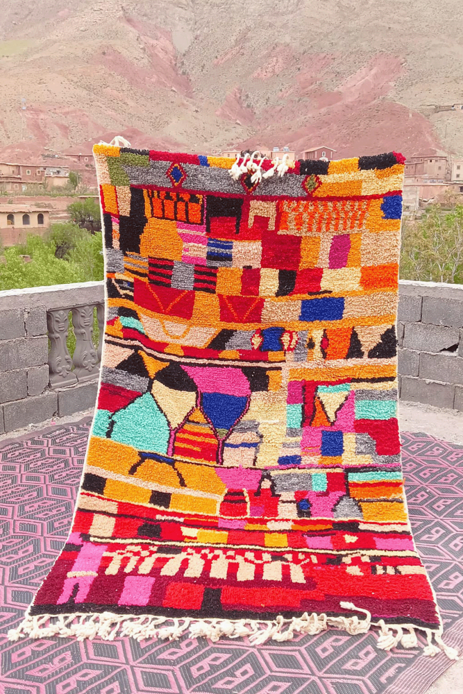 Tapis berbère coloré avec des motifs géométriques en rouge, bleu et orange sur fond clair.