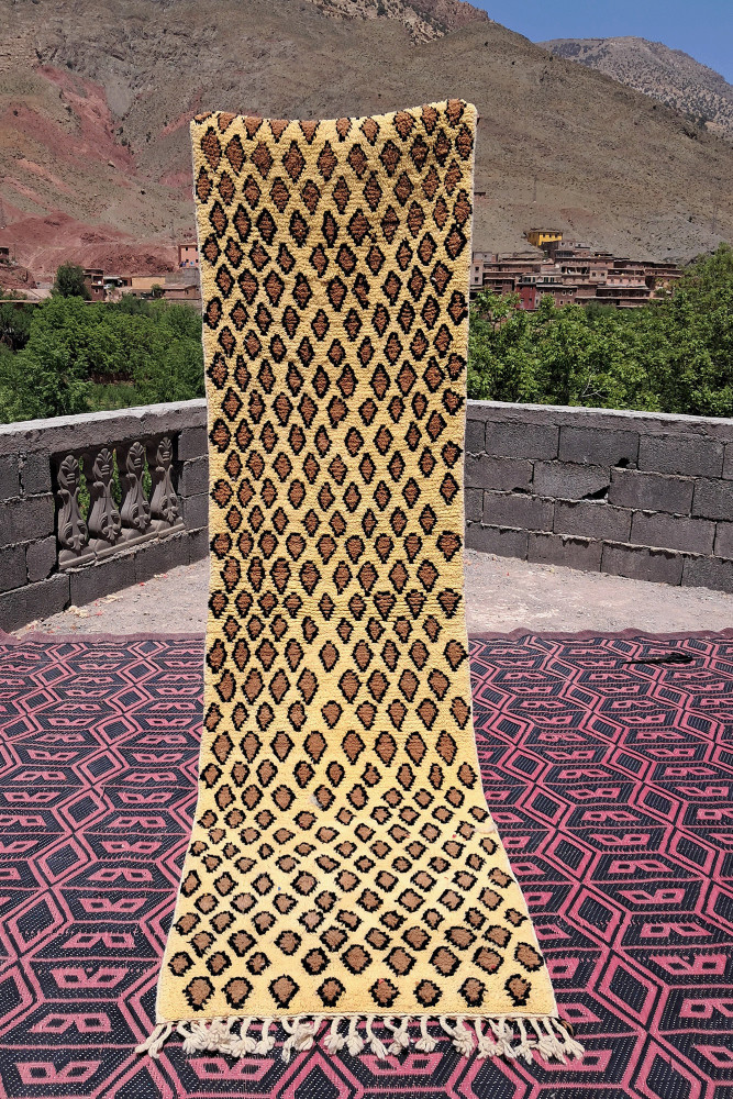 Tapis berbère en laine crème avec motifs géométriques noirs et marron, ajoutant une touche artisanale à votre décoration.