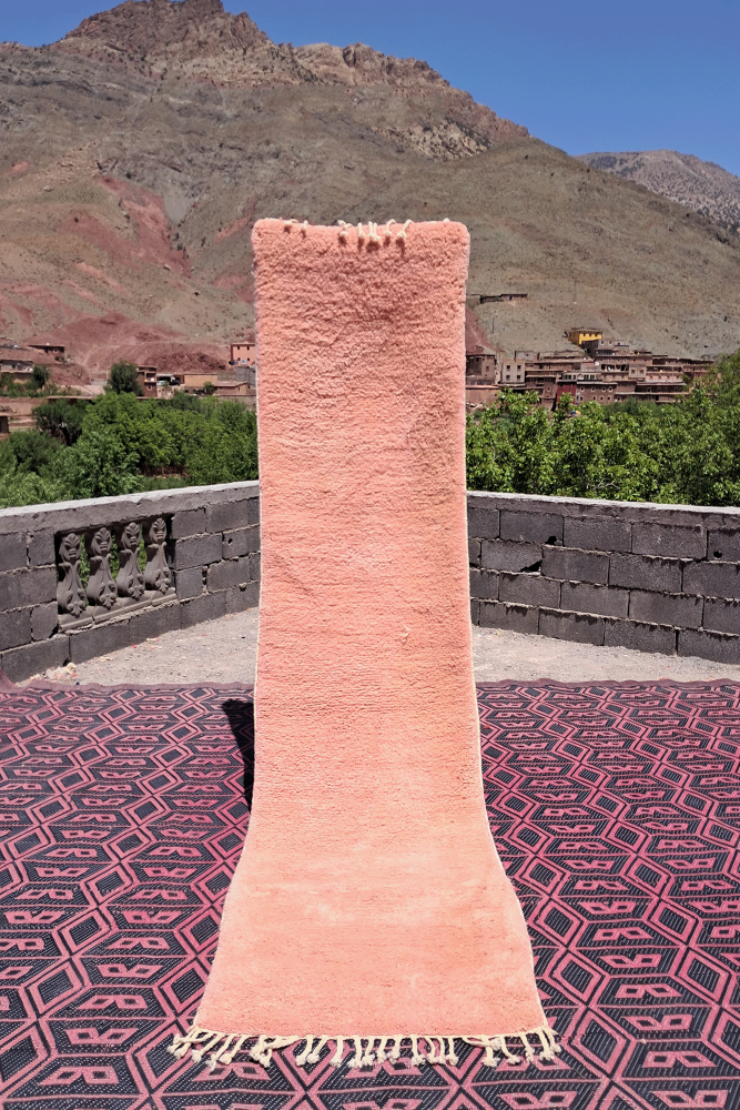 Tapis berbère en laine rose doux avec motifs géométriques sur fond noir, ajoutant une touche chaleureuse et moderne.