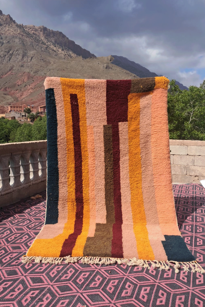 Tapis berbère aux couleurs vives avec des motifs géométriques et des bandes verticales en terracotta, orange et bleu.
