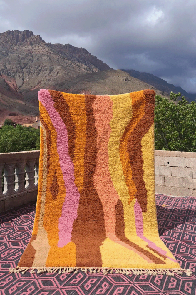 Tapis berbère aux couleurs chaudes et vives, avec des motifs abstraits en rose, jaune et orange.