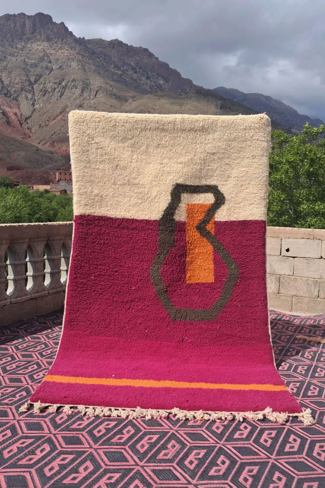 Tapis berbère en laine beige avec motifs géométriques en rouge et orange sur fond uni, apportant une touche artisanale moderne.