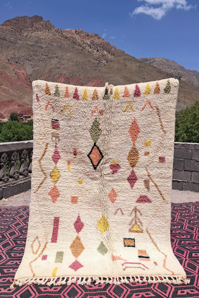 Tapis berbère artisanal aux tons neutres, motifs géométriques colorés en rose, bleu, jaune et verts.