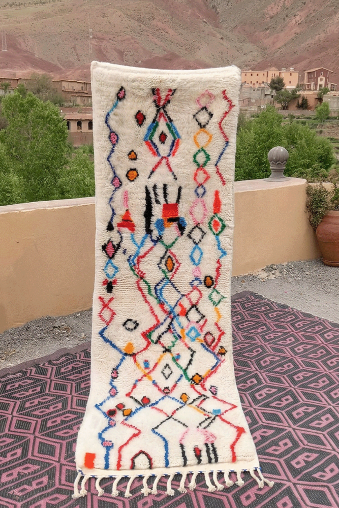 Tapis berbère aux motifs géométriques colorés, dominé par des nuances de blanc, bleu, rouge et noir.
