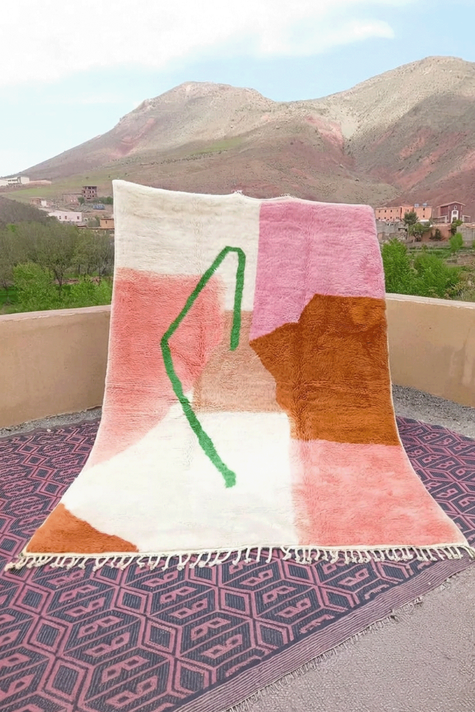 Tapis berbère aux couleurs pastel, motifs géométriques et touches de vert, rose et orange sur fond crème.