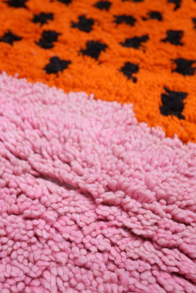 Tapis berbère aux motifs géométriques en orange, noir et rose, ajoutant une touche moderne et chaleureuse à la décoration.