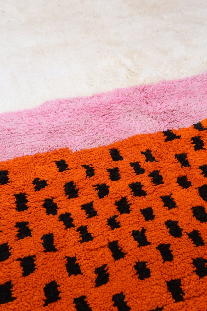Tapis berbère aux motifs géométriques, couleurs vives orange, noir et rose, ajoutant une touche moderne et chaleureuse.