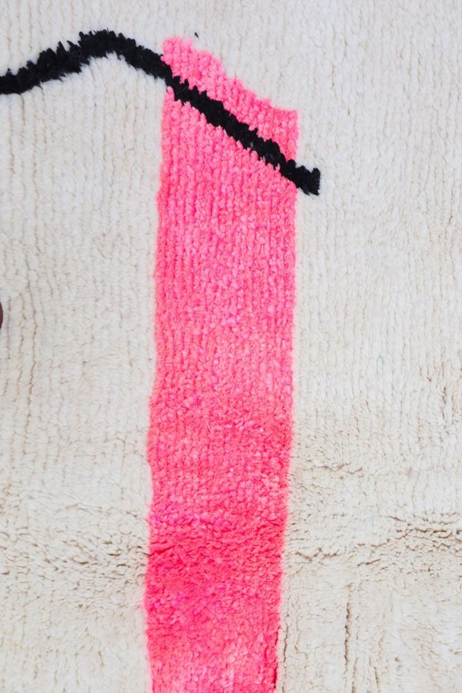 Tapis berbère aux motifs modernes avec des teintes de rose et de noir sur fond beige, parfait pour un décor contemporain.