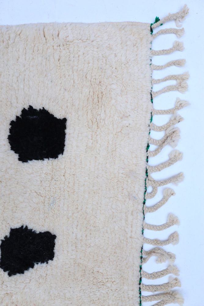 Tapis berbère doux en laine avec motifs géométriques noirs sur fond crème et franges naturelles.