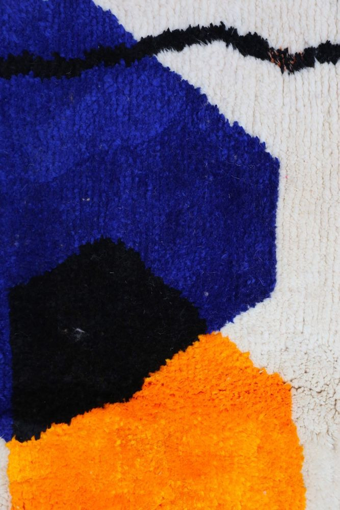Tapis berbère aux motifs géométriques colorés en bleu, noir et orange sur fond creme.