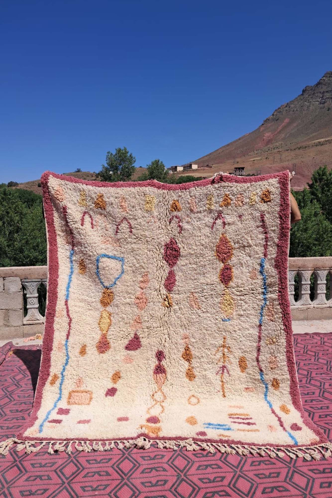 Berber-Teppich aus natürlicher Wolle, cremefarben mit geometrischen Mustern in Rosa, Blau und Gelb.