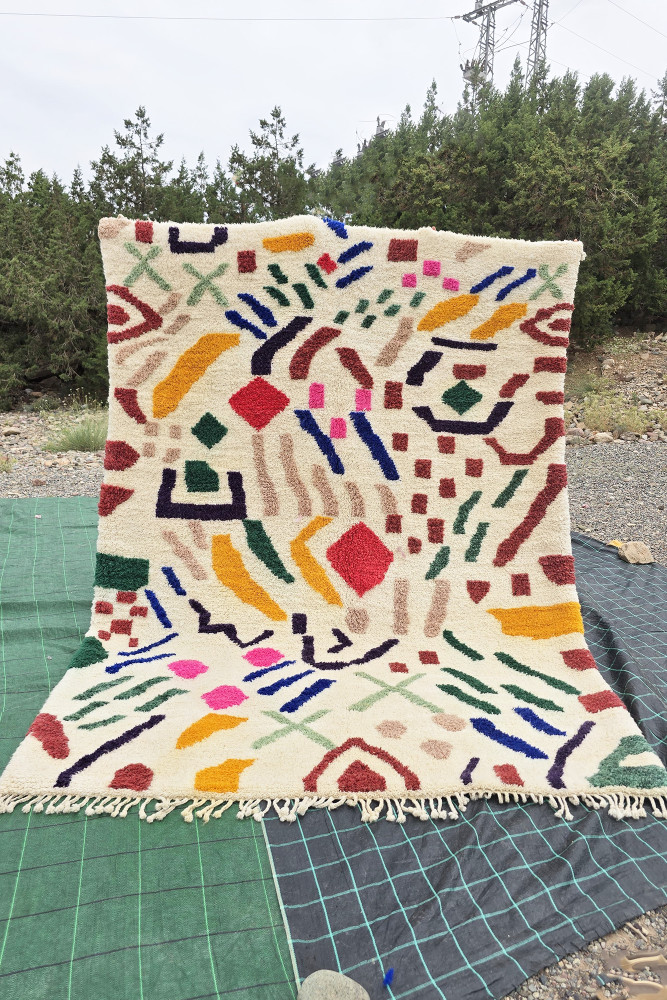 Tapis berbère aux motifs géométriques colorés, dominé par des tons crème, rouge, vert et jaune.