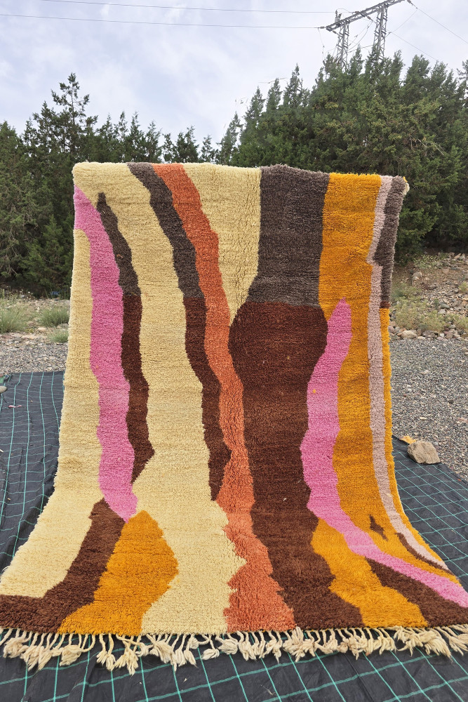 Tapis berbère aux motifs abstraits avec des couleurs chaudes telles que le beige, marron, rose et orange.
