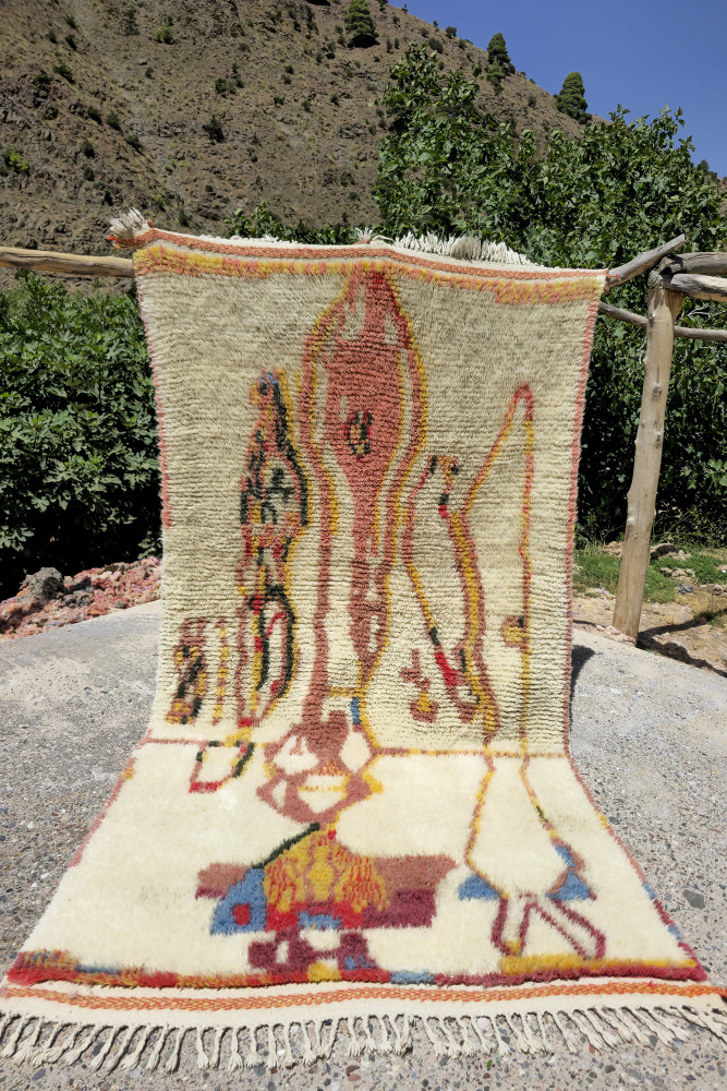 Tapis berbère aux motifs abstraits et couleurs naturelles dominées par le beige, le rouge et des touches de bleu.