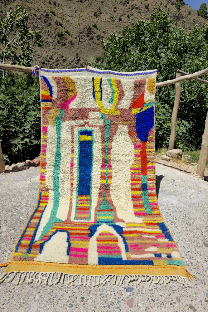 Tapis berbère coloré avec des motifs abstraits en bleu, orange, rose et crème sur un fond clair.