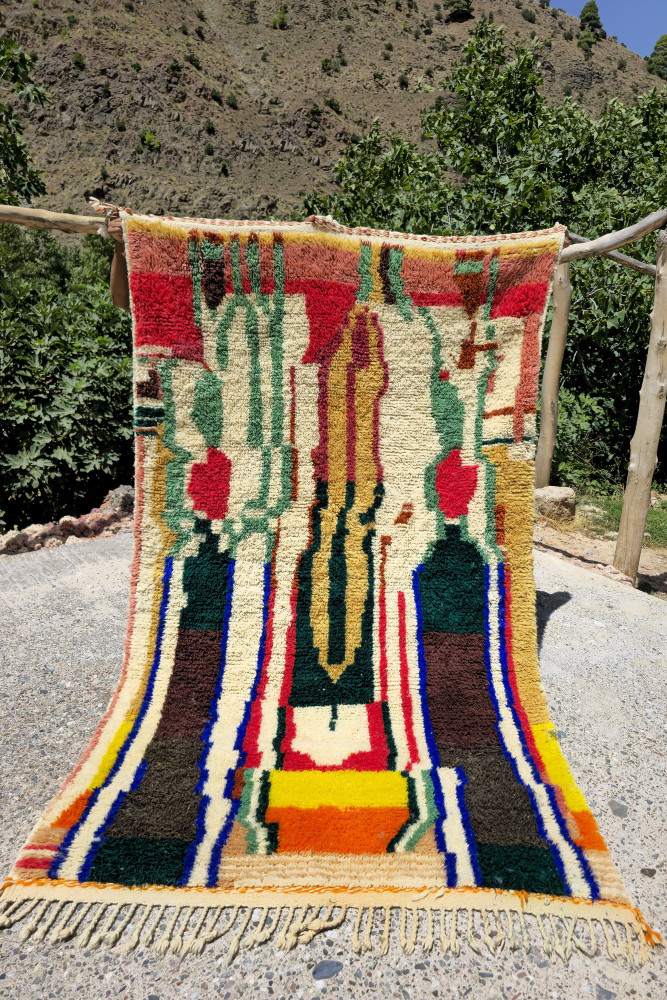 Tapis berbère coloré avec des motifs géométriques, dominé par des nuances de rouge, vert, et jaune.