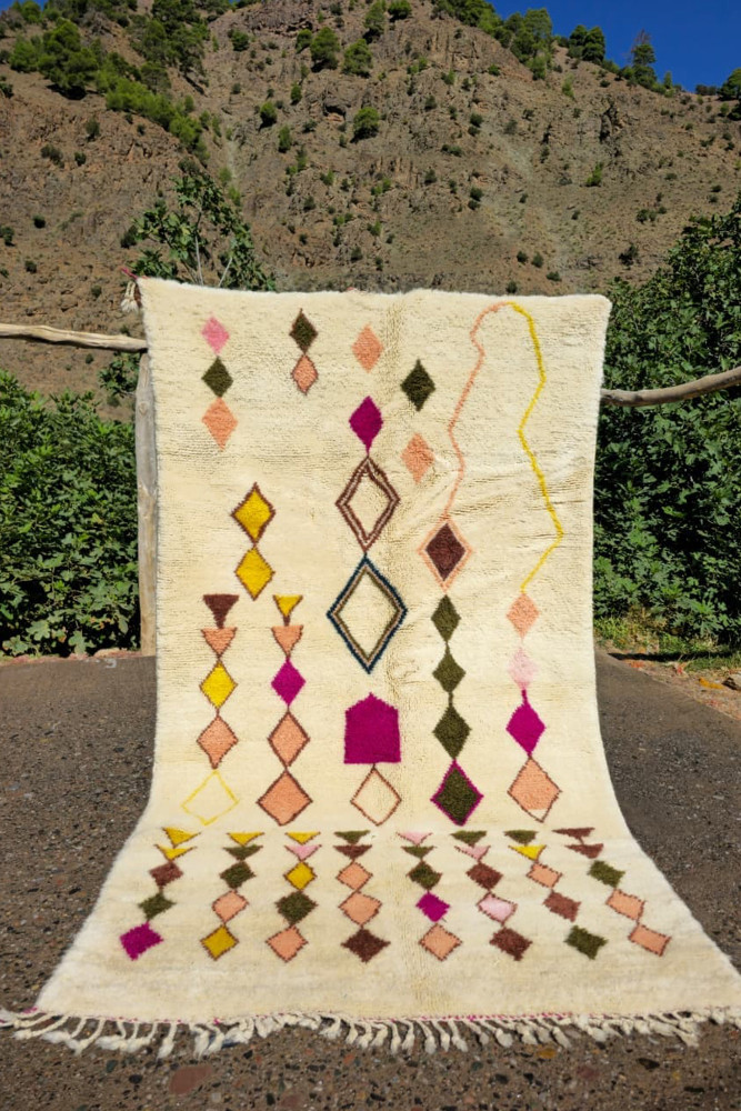 Tapis berbère aux motifs géométriques colorés, dominé par des teintes crème, rose, jaune et vert.