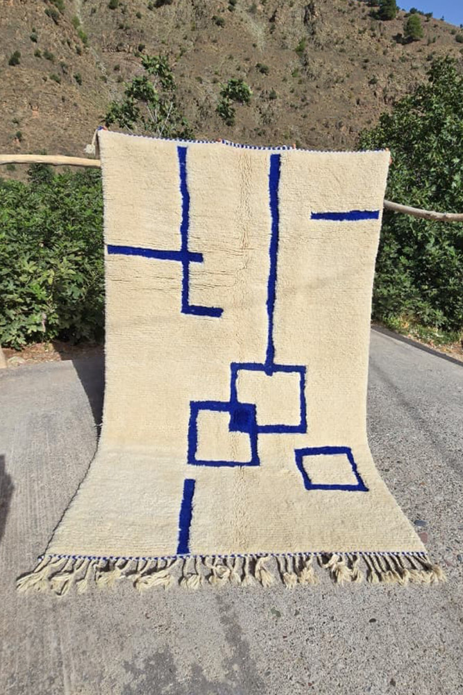 Tapis berbère blanc crème avec des motifs géométriques en bleu, parfait pour un décor moderne.