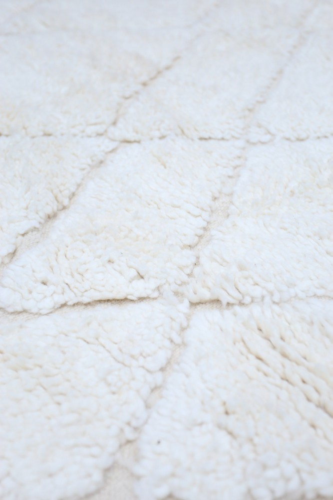 Tapis berbère aux motifs géométriques en blanc crémeux, offrant une texture douce et chaleureuse pour un intérieur élégant.