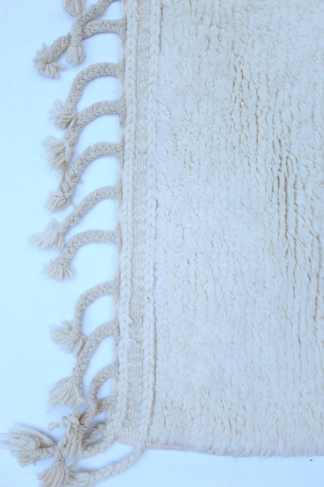 Tapis berbère en laine, couleur crème avec des franges tressées, design texturé et élégant pour un intérieur chaleureux.