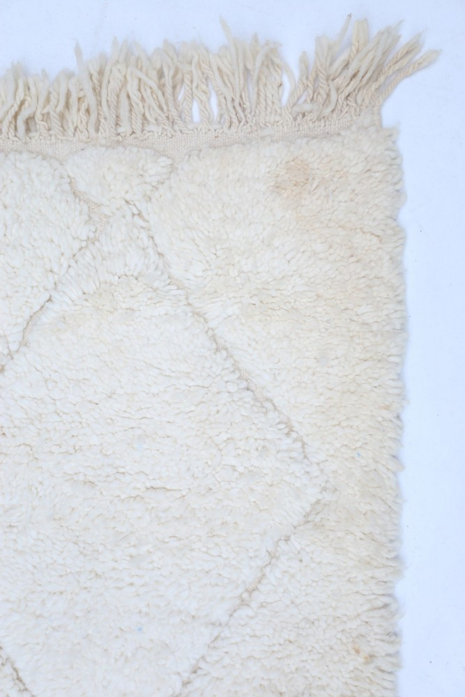 Tapis berbère en laine crème avec des motifs en losanges et des franges, apportant une touche chaleureuse et authentique.
