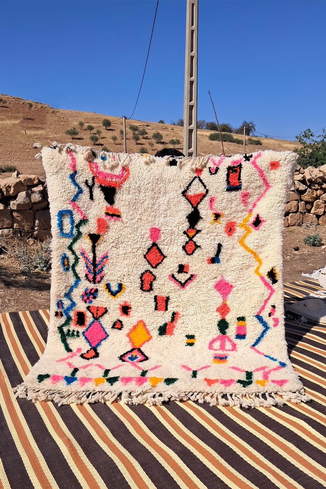 Tapis berbère haut en couleurs avec des motifs géométriques, dominé par le blanc, le rose, le bleu et le noir.