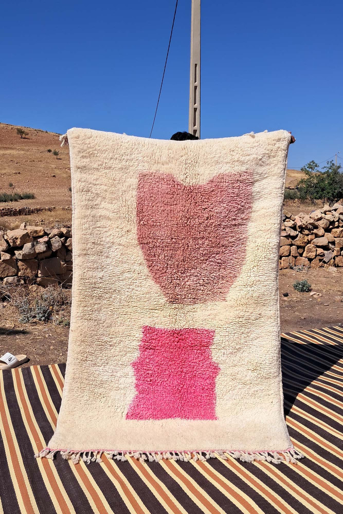 Tapis berbère en laine avec des motifs abstraits en rose sur fond crème, créant une ambiance moderne et chaleureuse.