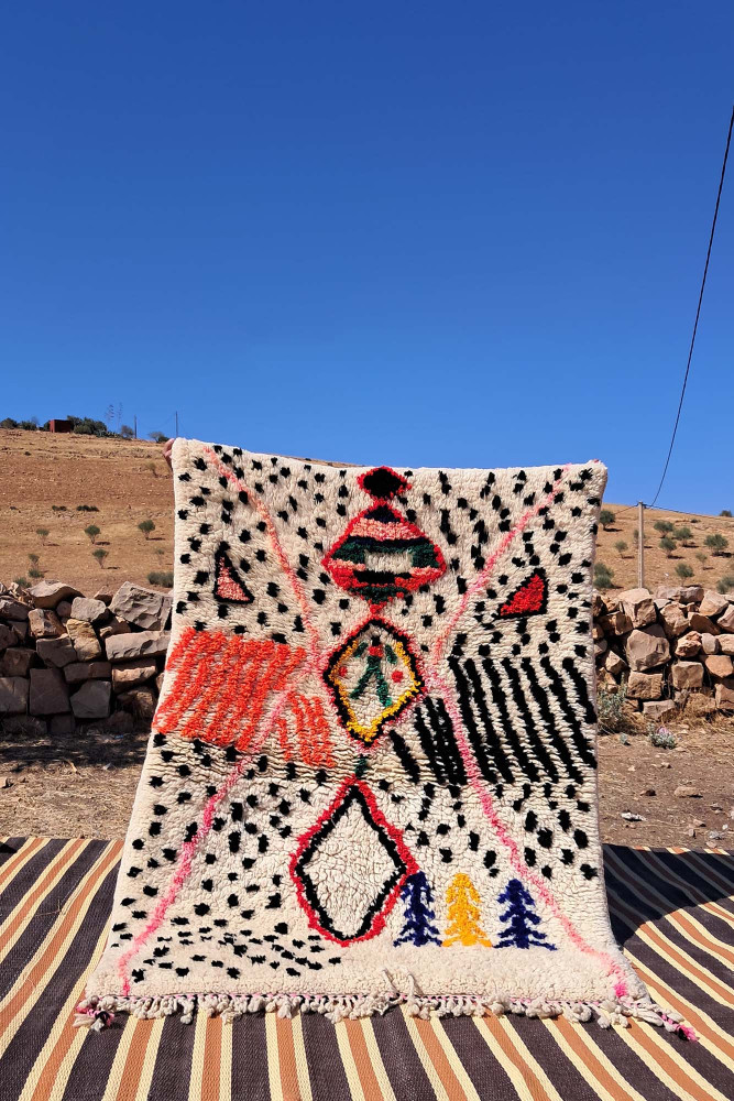 Tapis berbère aux motifs géométriques colorés, dominé par des teintes blanches, rouges et noires.