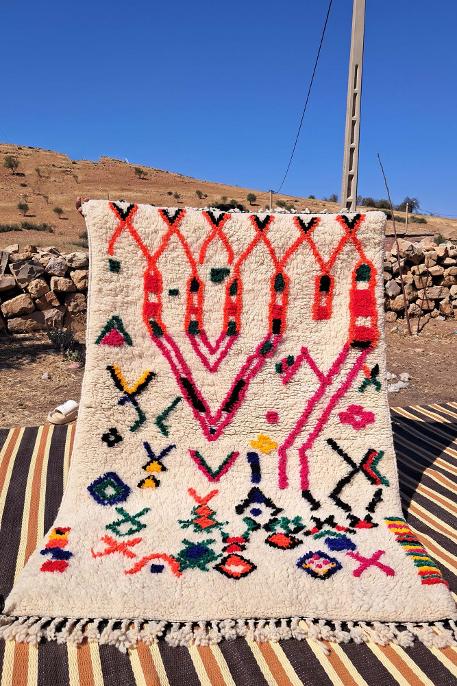 Tapis berbère en laine crème, ornée de motifs géométriques colorés en rouge, violet et vert.