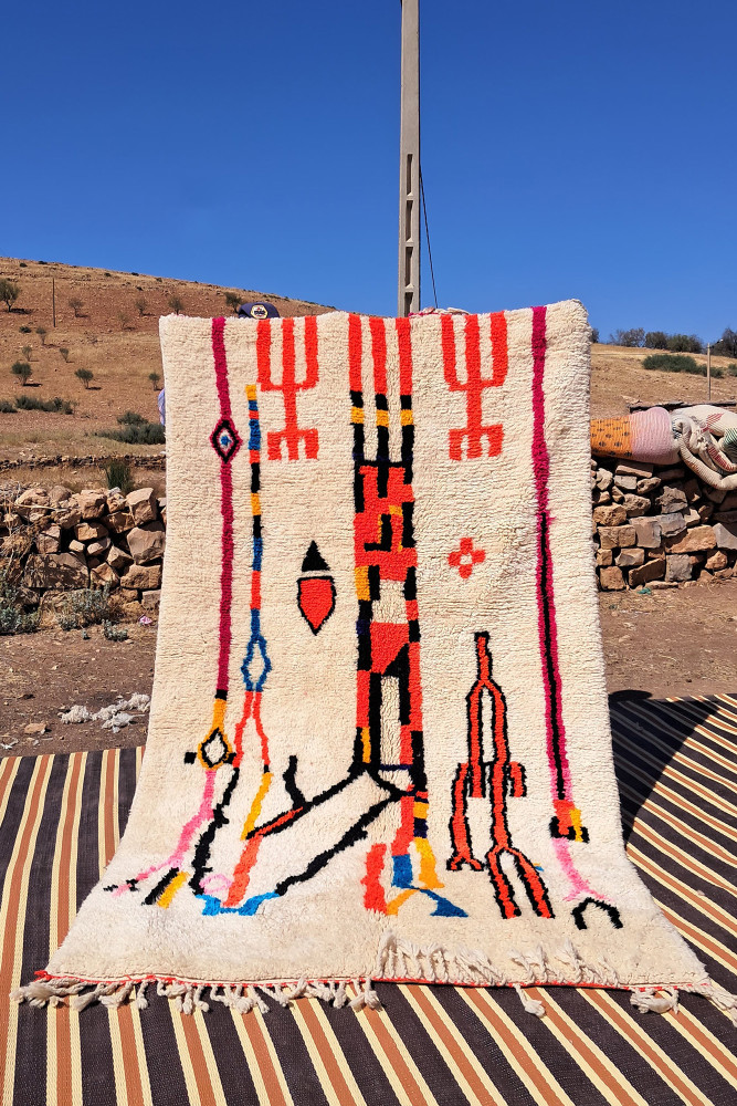 Tapis berbère au style coloré avec des motifs géométriques en rouge, bleu et noir sur un fond crème.