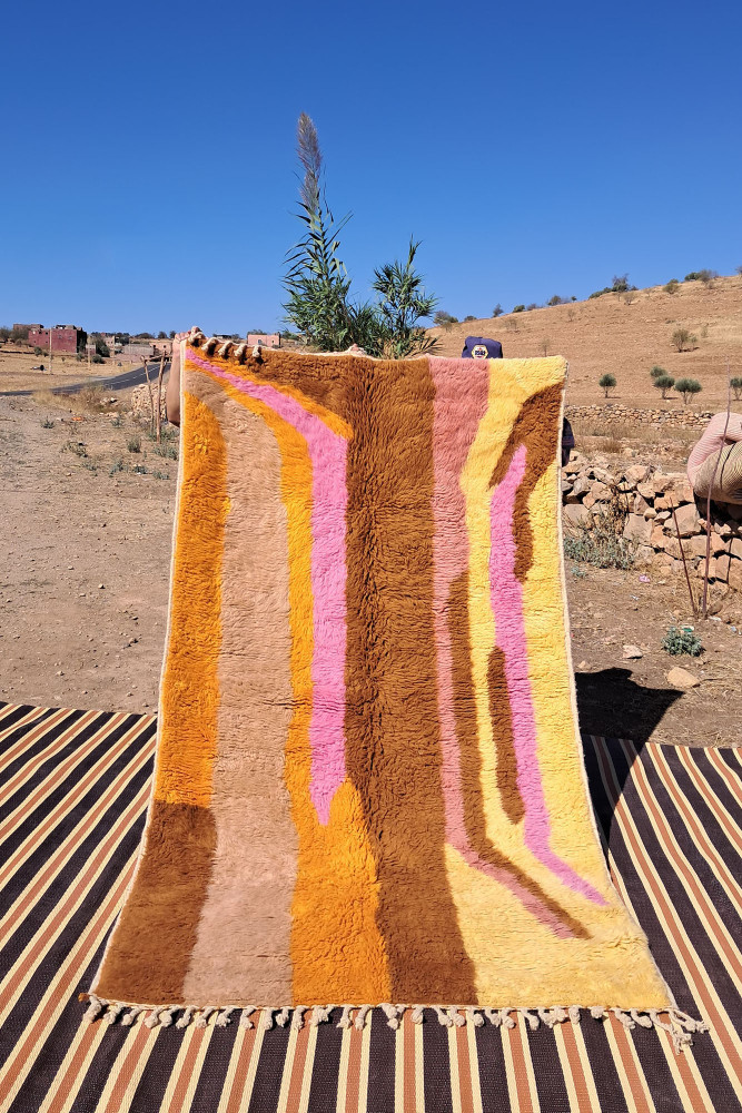 Tapis berbère aux couleurs vives de jaune, rose et brun avec des motifs ondulés modernes.