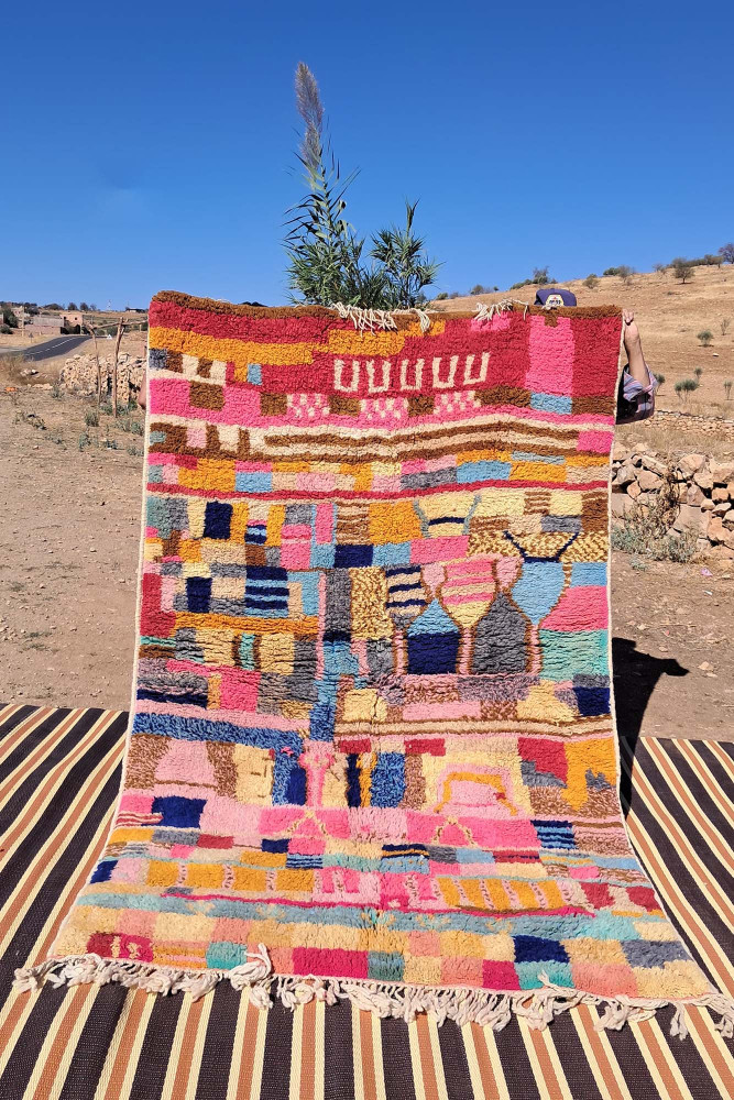 Tapis berbère coloré aux motifs géométriques vifs dans des teintes de rose, bleu, orange et beige.
