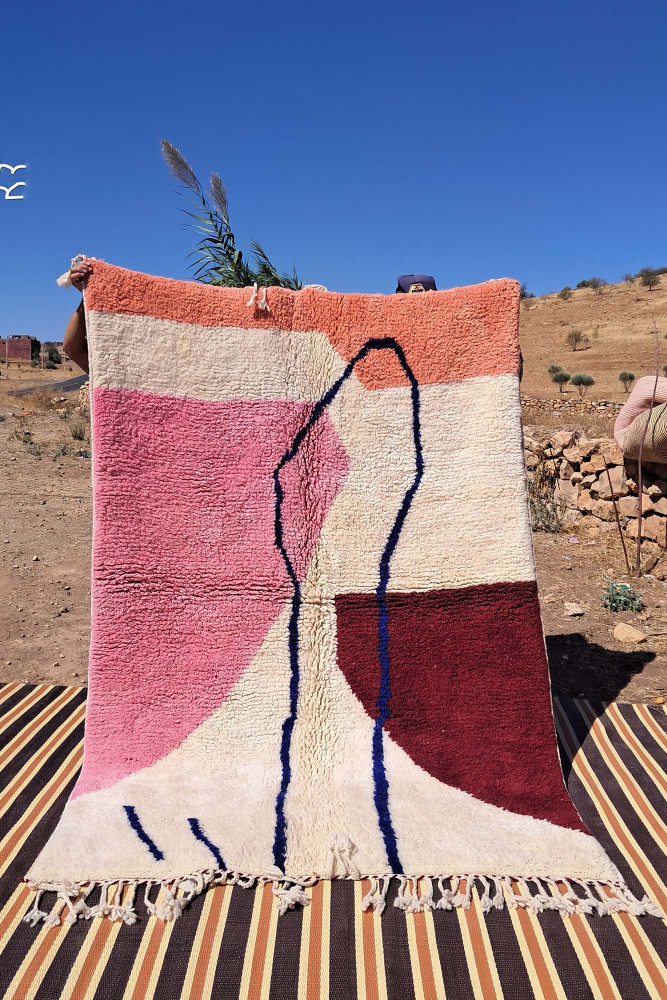 Tapis berbère au design abstrait, dominé par des couleurs rose, beige, rouge et bleu, avec des motifs géométriques.