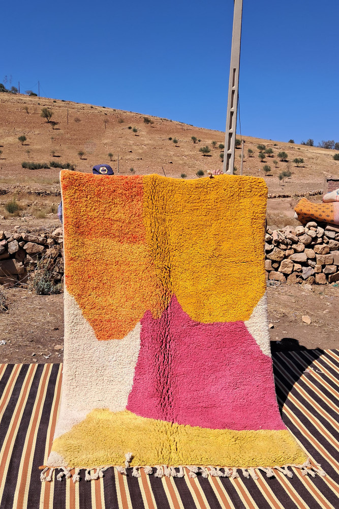 Tapis berbère aux couleurs vives avec des motifs géométriques en jaune, orange et rose sur fond crème.
