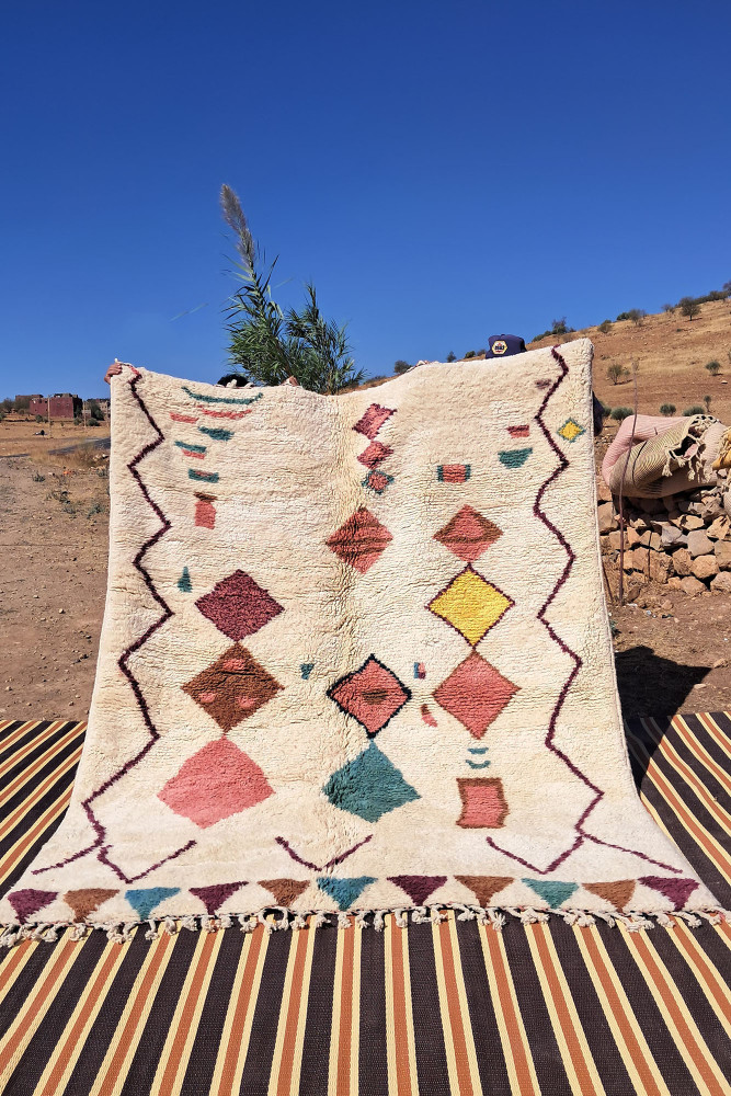 Tapis berbère avec motifs géométriques colorés en rouge, bleu, jaune et crème sur fond neutre.