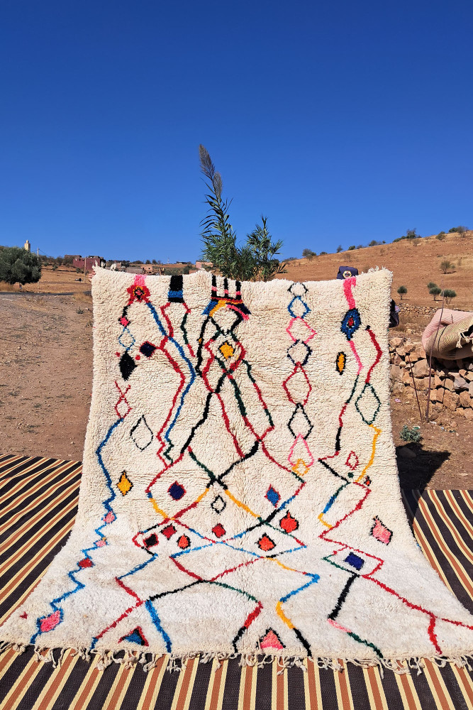 Tapis berbère en laine, couleur crème avec motifs géométriques colorés en bleu, rouge, jaune et noir.