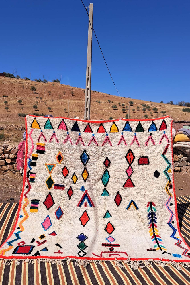 Tapis berbère aux motifs géométriques colorés, dominant le blanc, avec des touches de rouge, bleu et jaune.