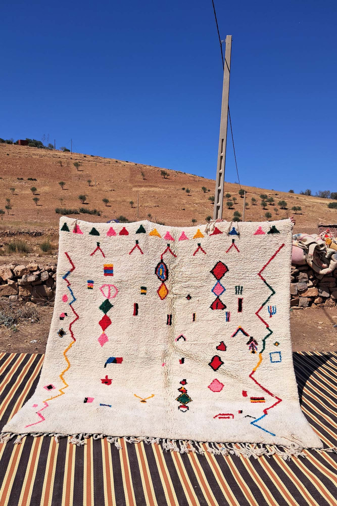 Tapis berbère en laine, aux motifs géométriques colorés sur fond crème, ajoutant une touche artisanale et chaleureuse.