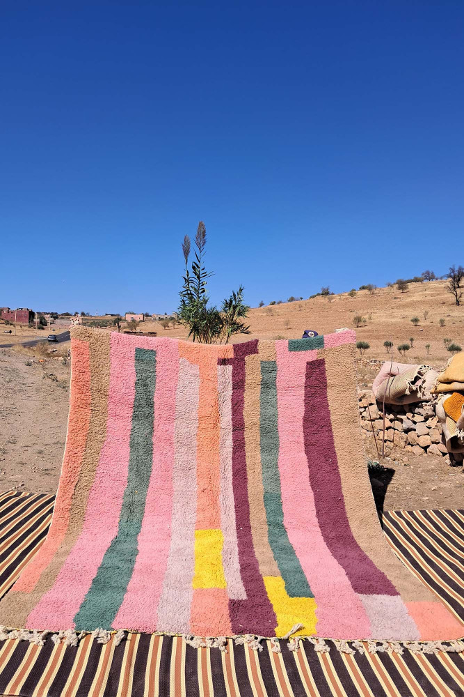 Tapis berbère aux couleurs vives avec des motifs de rayures roses, vertes et jaunes sur fond beige.