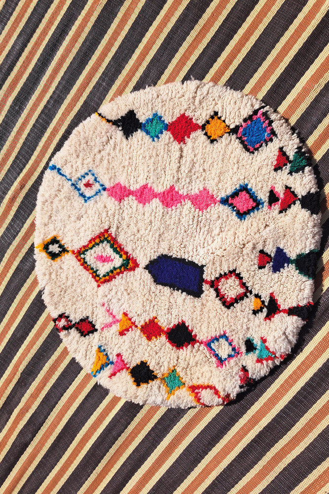 Tapis berbère rond en laine, motifs géométriques colorés sur fond crème, ajoutant une touche artisanale à votre décoration.